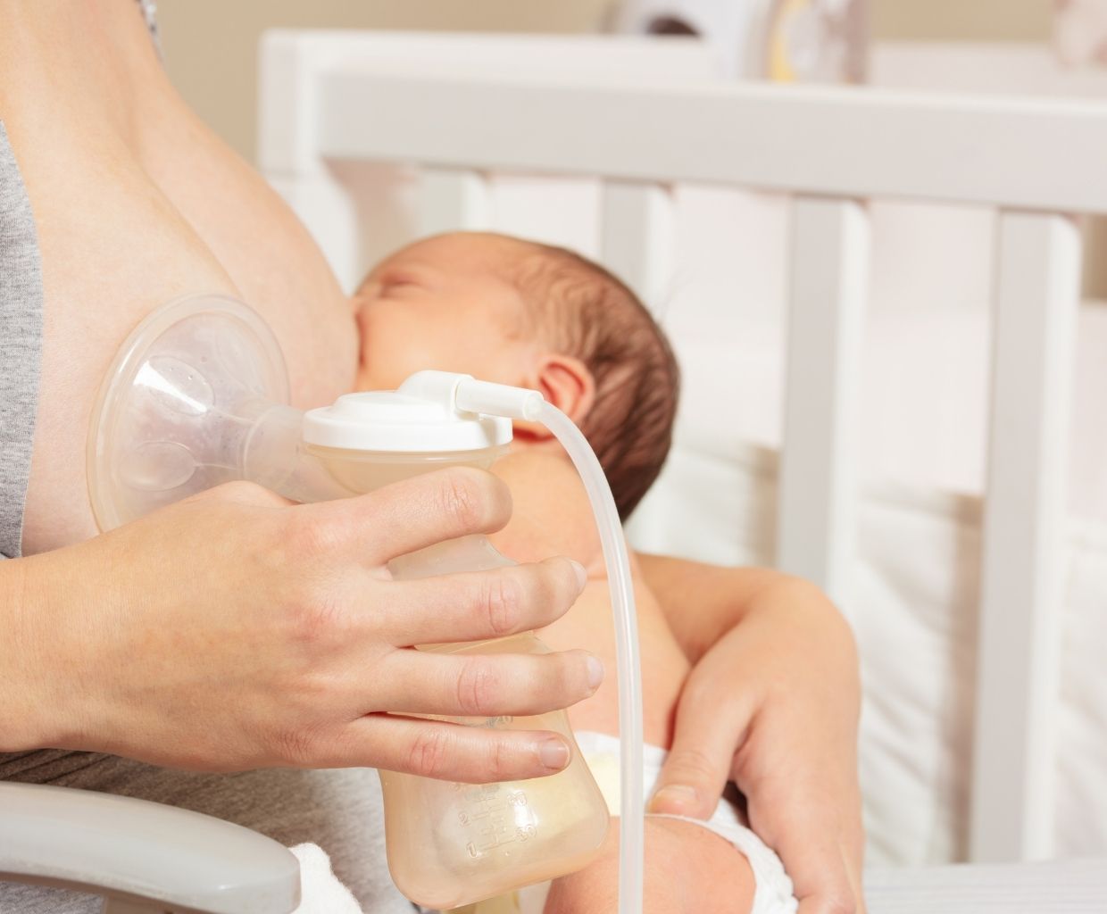 Mother pumping golden-yellow breast milk into a bottle while holding her sleeping newborn