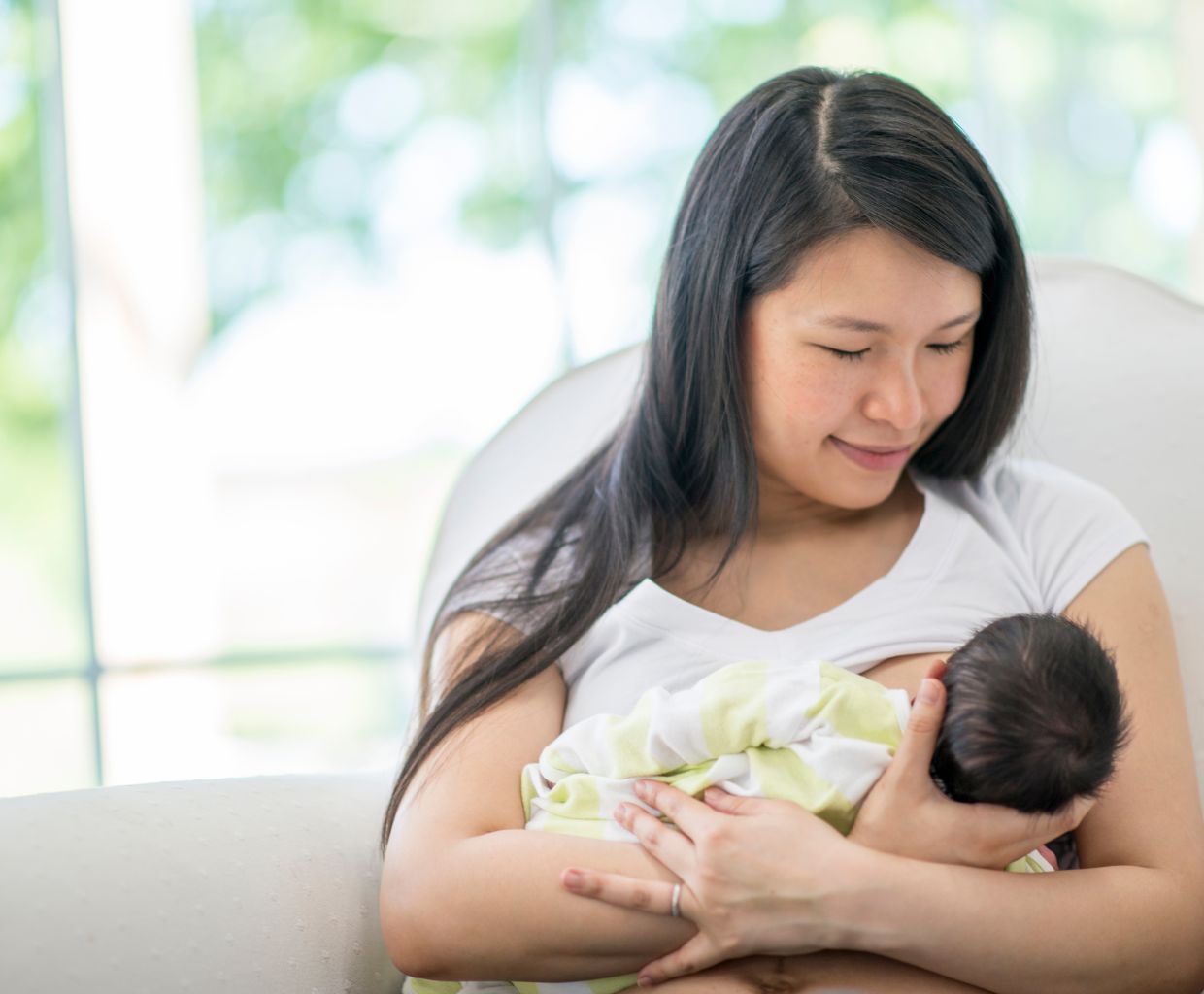 Mother smiling with her eyes closed as she breastfeeds her newborn wrapped in a striped blanket