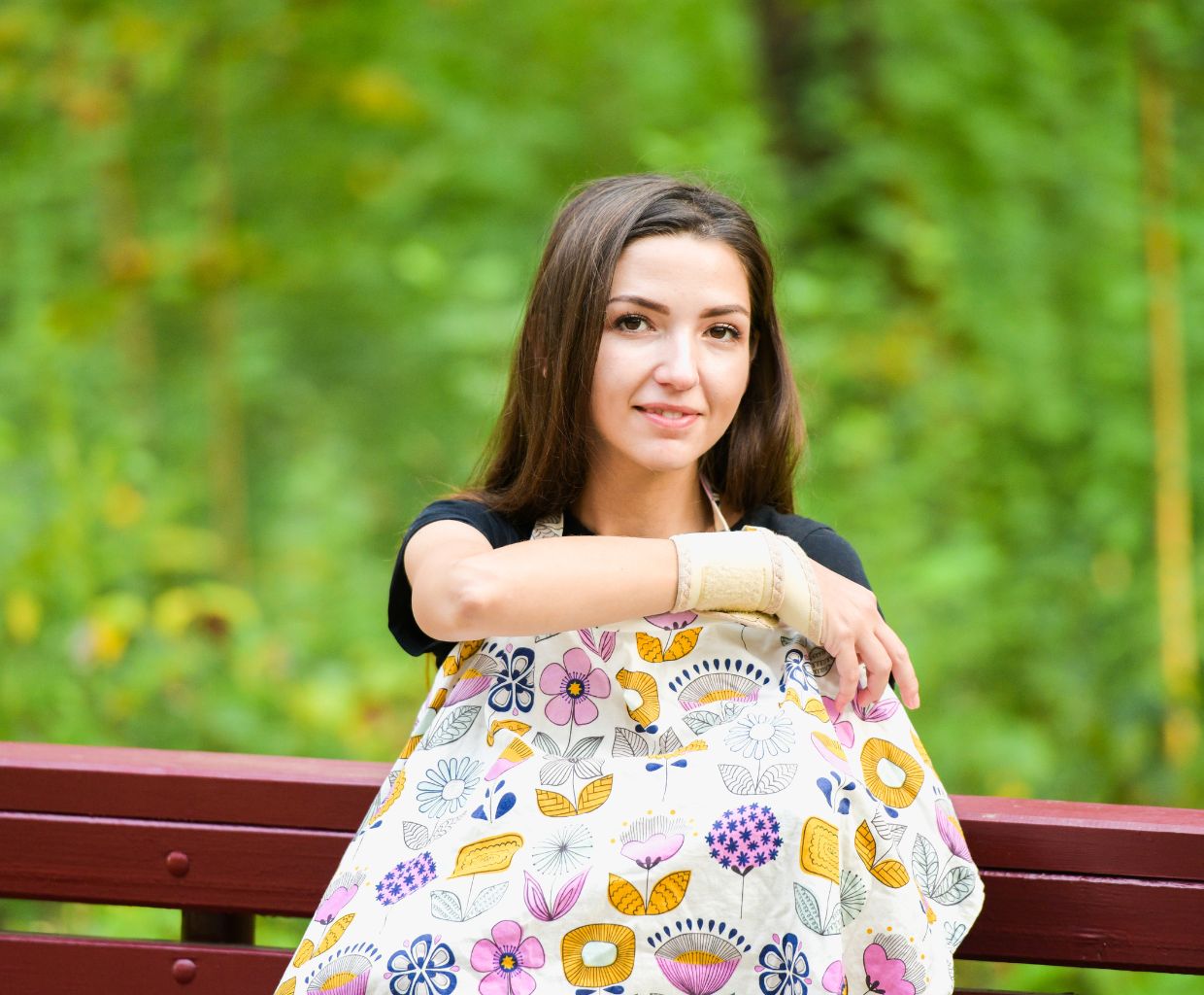 Smiling woman on a park bench wearing a white floral nursing cover over her front