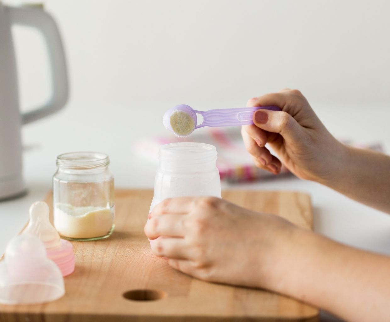 Parent spooning powdered infant formula into a baby bottle on a wooden board