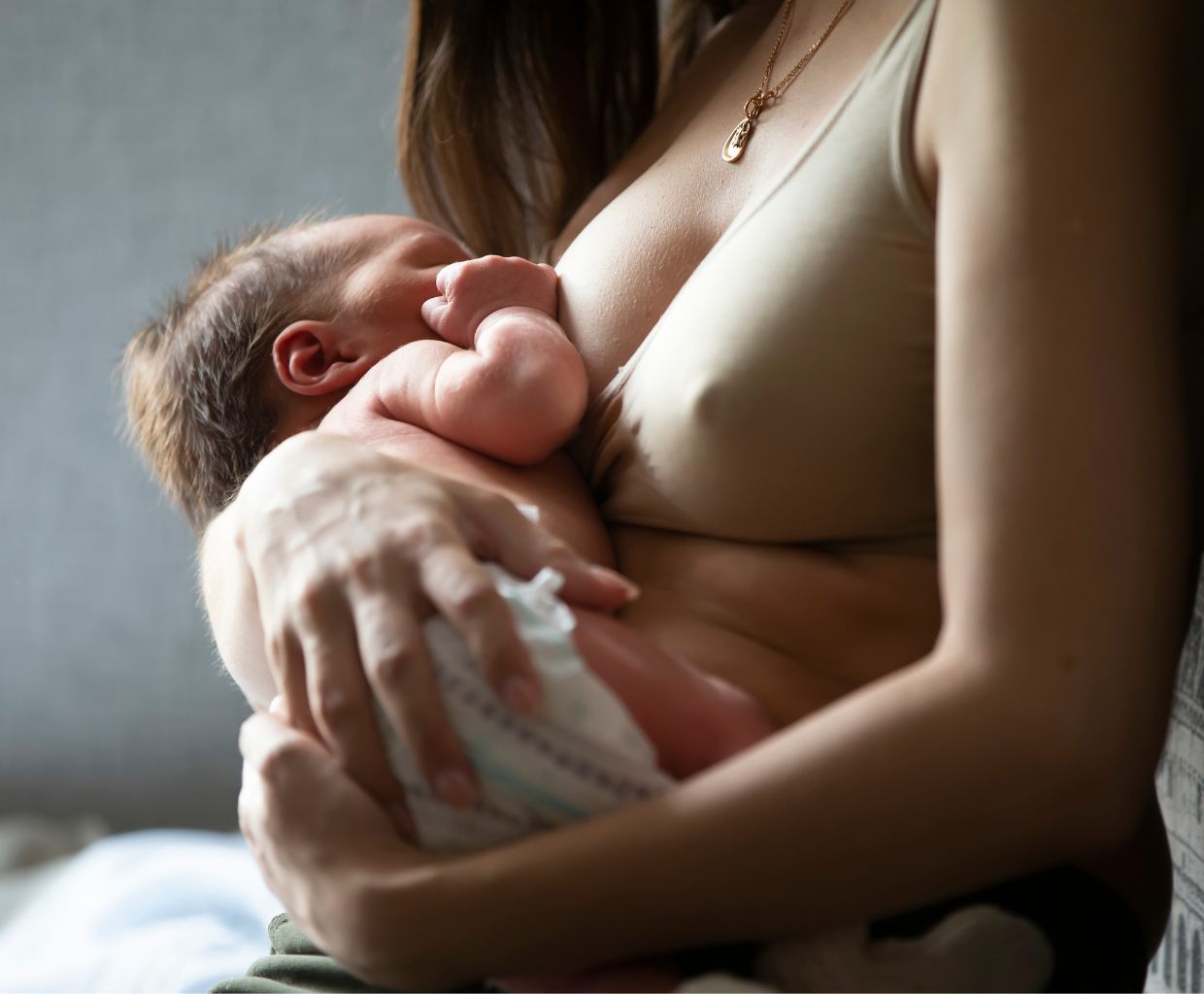 Mother in a beige nursing bra breastfeeding her newborn baby close to her chest