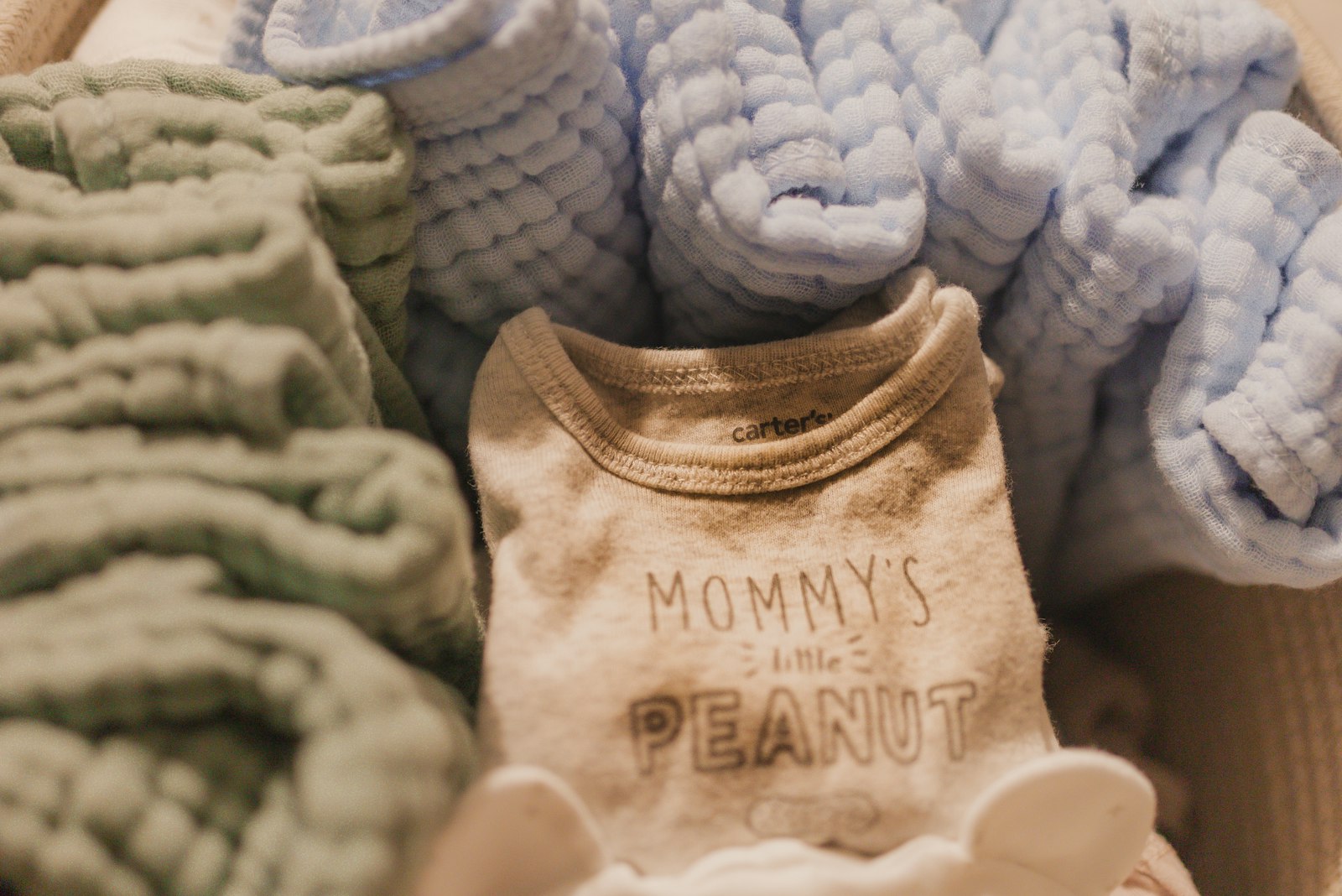 Folded baby clothes and a onesie in a woven basket