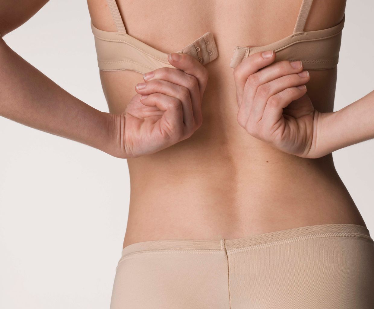 Woman fastening the clasp of a plain, supportive bra, seen from behind