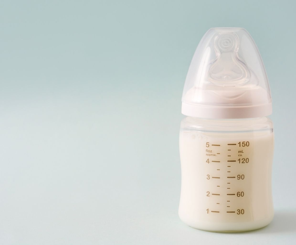 Baby bottle filled with breast milk, with measurement markings, against a pale blue background