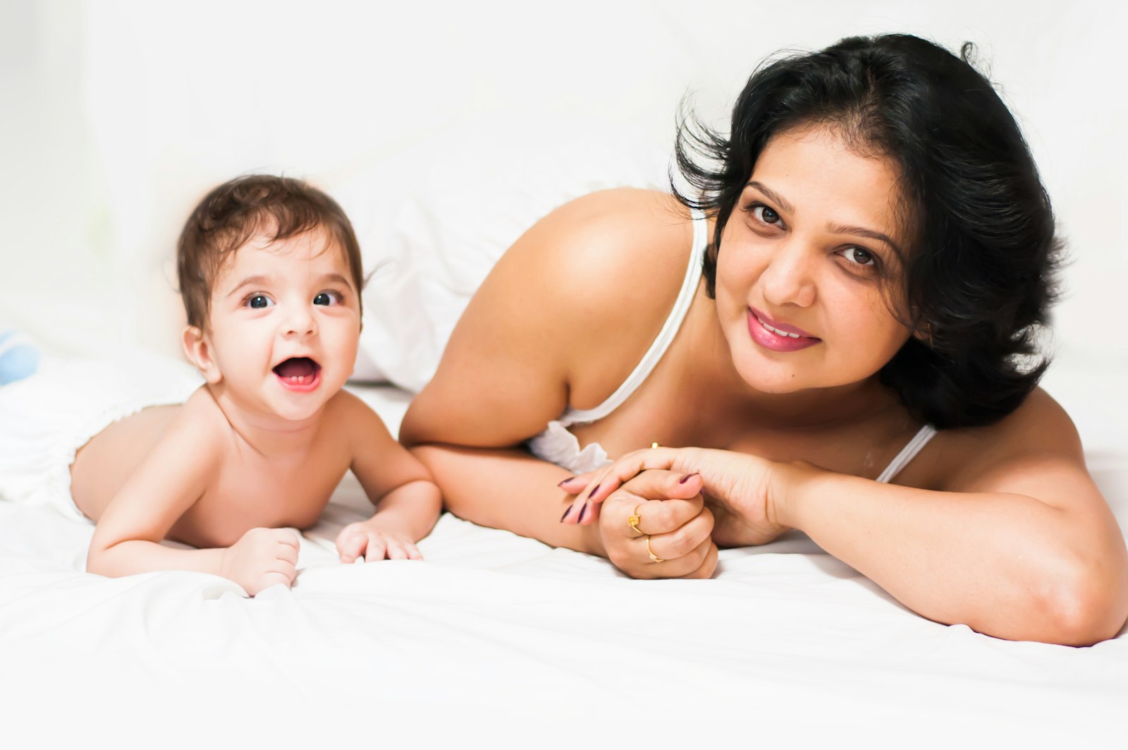 Mother and baby lying side by side on a white bed, smiling