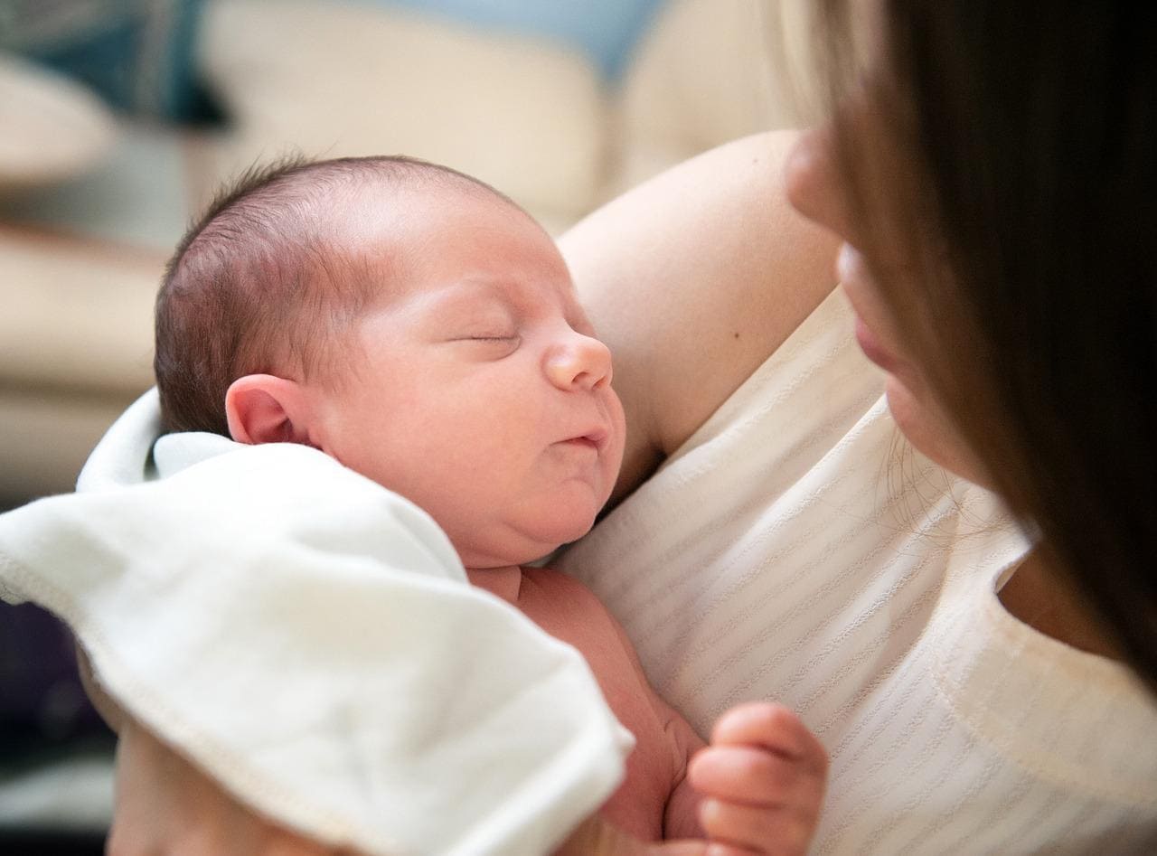 Mother holding her sleeping newborn wrapped in a white blanket close to her chest