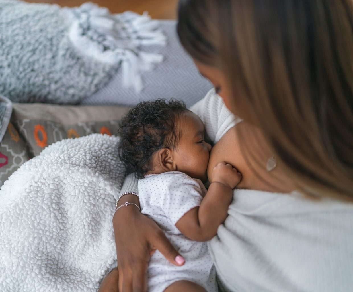A mother breastfeeding her baby on a soft blanket at home